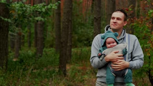 Young Father with His Newborn Baby in a Sling Walking in the Autumn Forest The Concept of a Happy