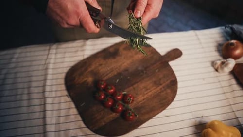 Hands Cutting Rosemary with Scissors over Tomatoes
