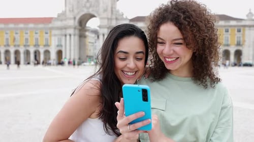 Two Women Looking at Phone and Smiling in City