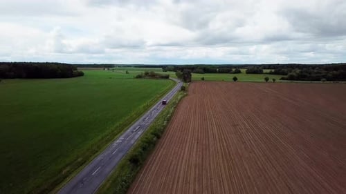 Aerial landcape shot following a red van driving on road agricultural area cloudy weather zala count