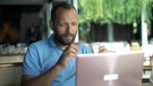 Young Man Using Laptop and Drinking Cocktail Sitting in Cafe 30s