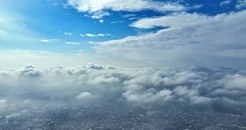 Aerial drone footage flying above the clouds with a snow is covering city landscape visible below
