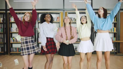 Grupo de jovens estudantes multirraciais comemorando alegremente em uma biblioteca enquanto jogam dólares