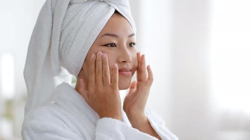 Woman Massaging Face in Bathroom in White Robe