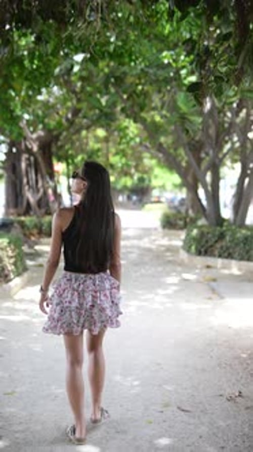 A Woman Peacefully Walks in a Green Park Enjoying the Beauty of Nature on a Sunny Day
