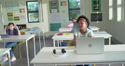 On teacher cue African American teen raising hand, placing laptop and headset, answering in class