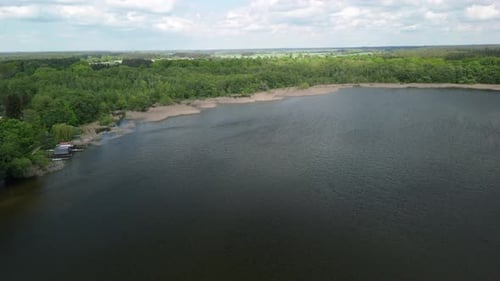 Aerial footage of a tranquil lake surrounded by lush green forest. The calm water reflects the sky,