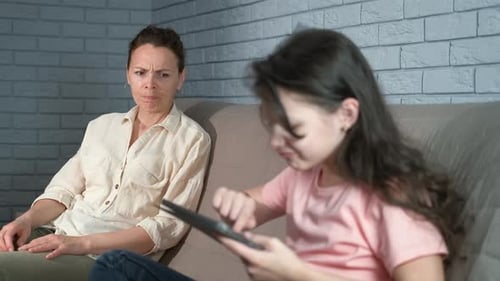 Woman Frowning at Child Using Tablet on Couch