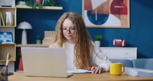 Woman Working on Laptop and Writing in Notebook