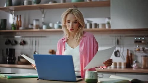 Woman Reviews Documents and Works on Laptop in Kitchen