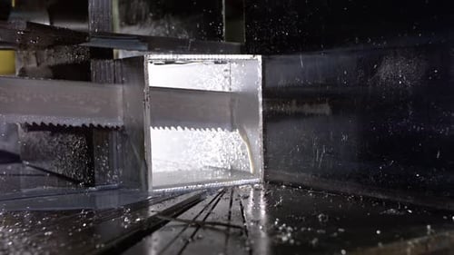 Bandsäge beim Sägen durch ein aluminiumförmiges Rohr mit Kühlflüssigkeit in Superzeitlupe 800 Bilder pro Sekunde