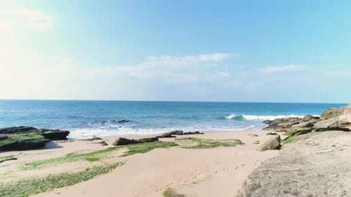 Flying forward over a rocky sand beach towards the blue azure sea water in Cadiz, Spain