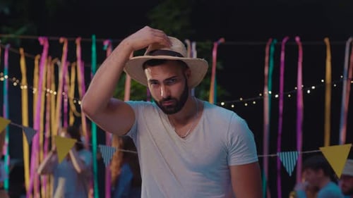 Man Adjusts Straw Hat at Outdoor Party at Night