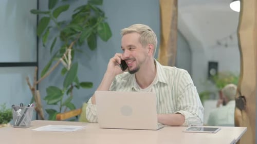 Young Man on Smartphone Call at Office Desk
