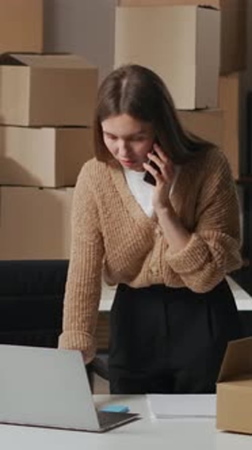 Young Entrepreneur Managing Online Store Orders in Small Office Workspace Talking on Phone While