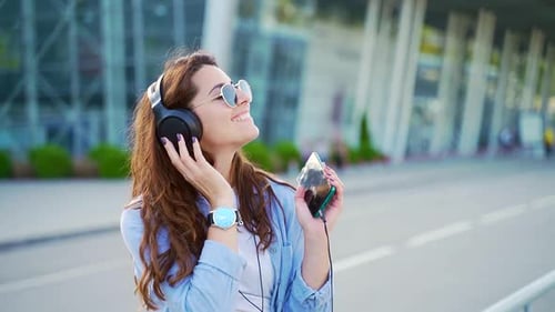 Portrait of cheerful young woman using headphones and modern smartphone for listening music