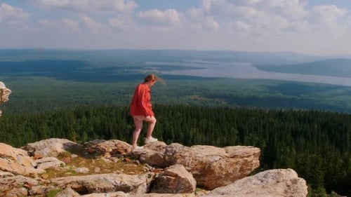 Young Woman Standing on the Edge of Mountain and Looking at the Forest