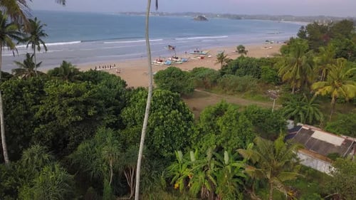 Aerial dolly tilt of beach in Weligama, Sri Lanka with fishing boats in the background.