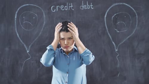 The woman writing Loan Debt looks on the blackboard with a sad expression.