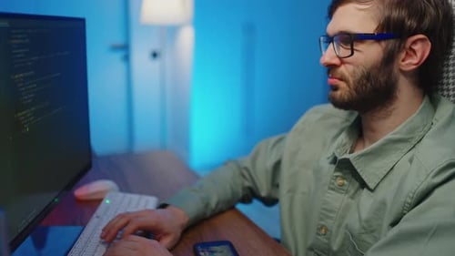 Young adult typing code on computer at desk