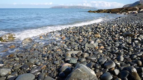 Sunny blue ocean waves wash over stone pebble beach coastline island holiday scene left dolly