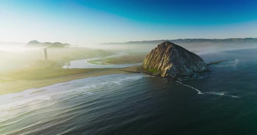 Magical sight of Morro Bay covered with thick fog. Triangle rock at the shore of Central coast