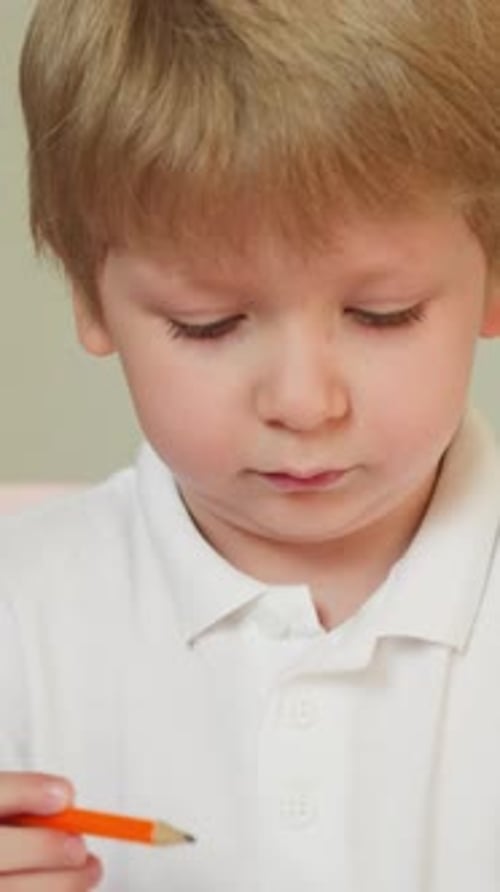 Toddler Examines Pencil and Draws Picture Sitting at Table