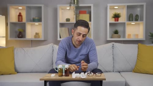 Man Blows Nose With Cold on Couch Indoors