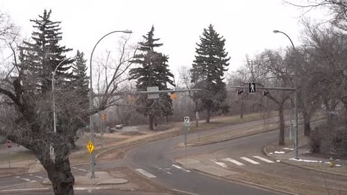 Intersection with some vehicles passing and very few people walking on the sidewalk with ligh snow f