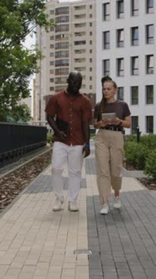 Vertical of Coworkers Walking in Park and Discussing Business Issues