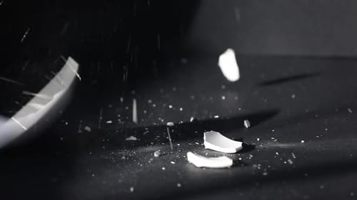 Porcelain cup falling onto saucer and breaking on black background, closeup