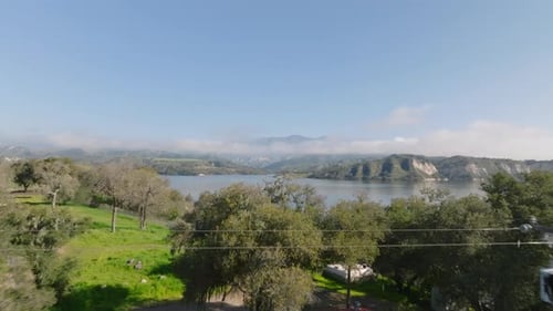 Forwards Fly Above Trees Revealing Lake with Cliffs on Opposite Bank and Mountains in Background