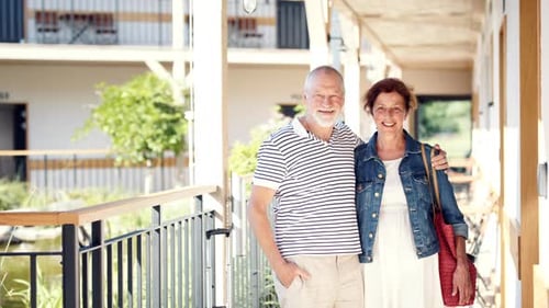 Senior Couple with Luggage Outside Apartment on Holiday, Looking at Camera
