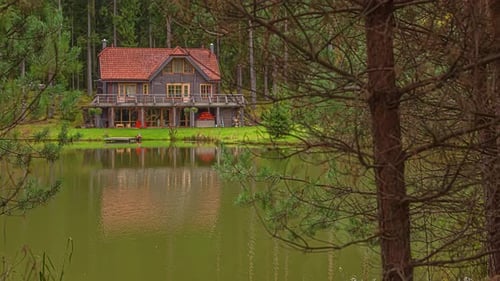 Tilt down shot of beautiful lakeside lodge along spring landscape beside a lake in timelapse.