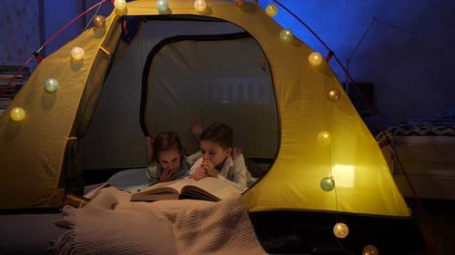 Children Reading Book Together in Tent at Night
