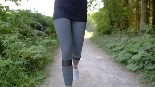 A woman wearing athletic apparel jogging in a park setting. TILT UP from her white shoes to reveal h
