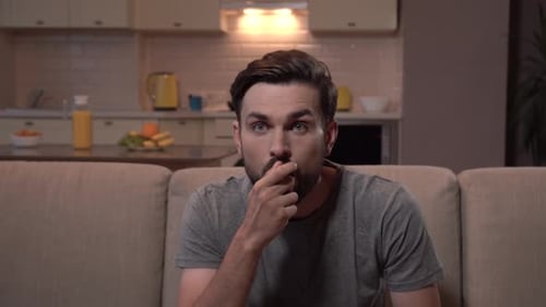 Shocked Man Sitting on Couch Reacting
