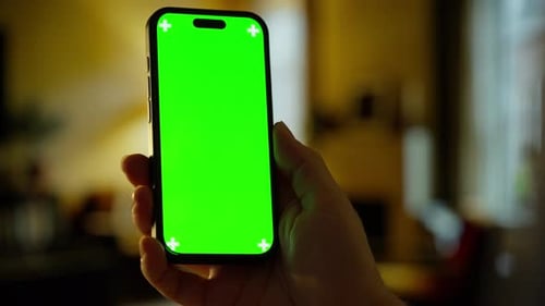 Person Holding Modern Smartphone with Bright Green Chroma Key Screen in Warm Indoor Environment for