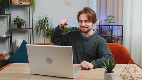 Man Celebrates Success at Laptop in Home Setting