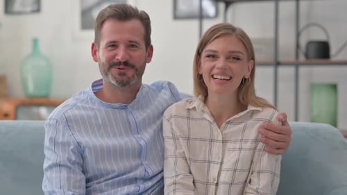 Smiling Couple Waving to Camera While Sitting on Couch