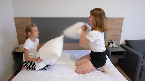 Famille heureuse de maman et mignonne petite fille jouant à une bagarre d'oreillers sur le lit, mère joyeuse riant
