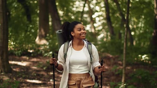 Woman Hiking in the Forest With a Backpack and Trekking Poles During the Daytime
