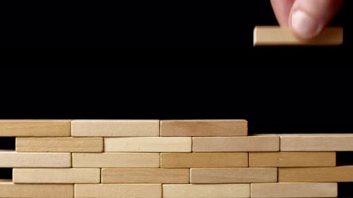 Eine Hand legt einen Holzklotz an die Wand. Das Konzept der Projektplanung in der Wirtschaft.
Konstruktion