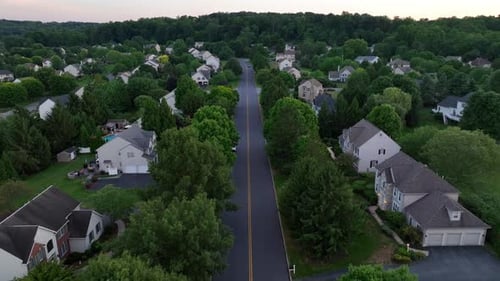 Leere Hauptstraße mit grünen Bäumen in amerikanischen Vororten bei Sonnenuntergang. Amerikanische Einfamilienhäuser w
