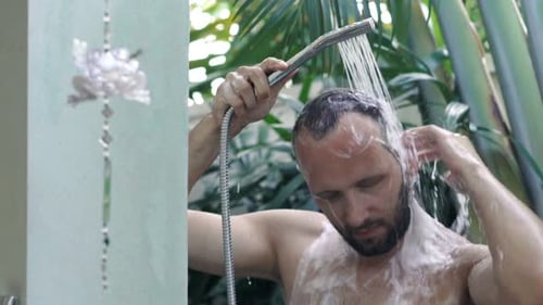 Man shampooing hair in outdoor tropical shower
