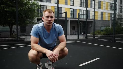 A Man Sits on a Sports Field and Looks at the Camera