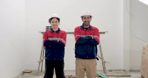 Asian woman engineer and male contractor stand inside unfinished building, gesturing during