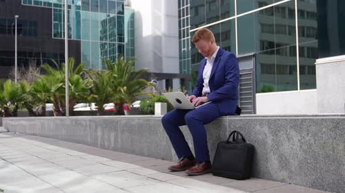 Man Works on Laptop and Phone Outside Office