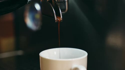 A medium close up of coffee pouring from a coffee into a white cup.