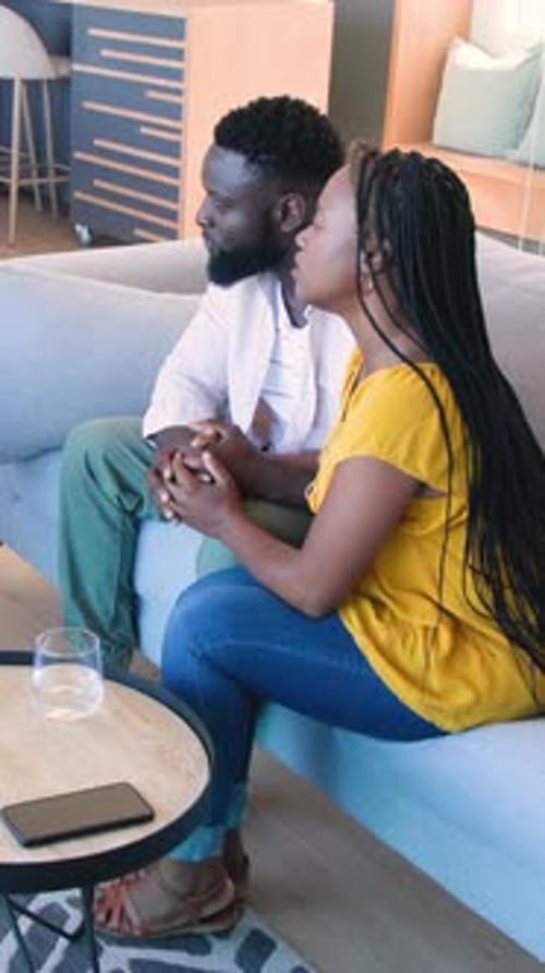 Vidéo verticale : couple afro-américain sur un canapé discutant d'un plan, examinant le bloc-notes, écrivant des notes